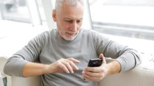 focused mature man typing on cellphone while sitting