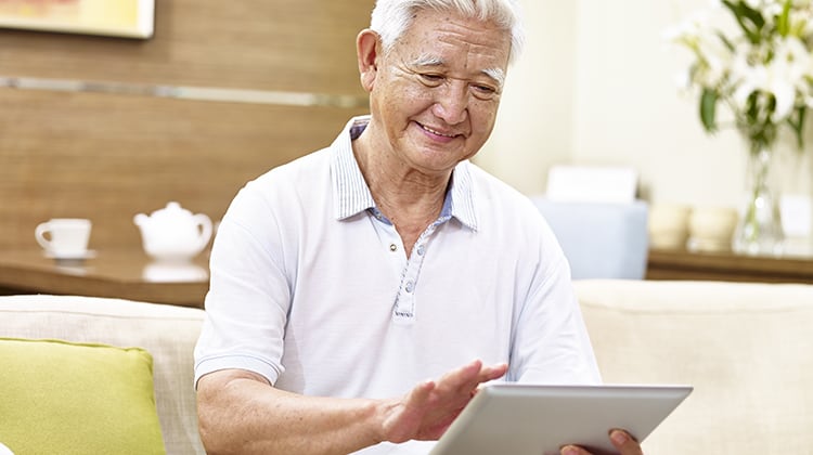 active senior asian man sitting on couch using tablet computer, relaxed, smiling